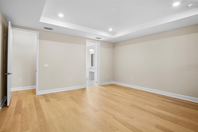 empty room featuring a tray ceiling and light hardwood / wood-style floors