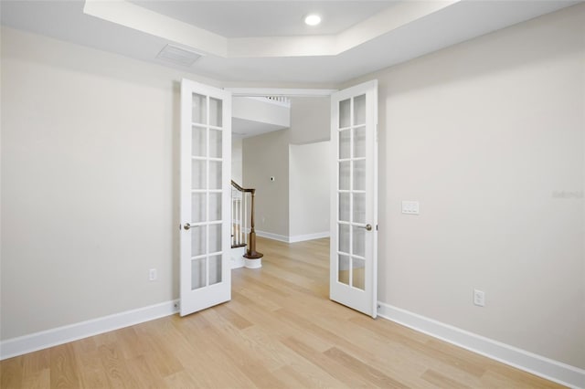 empty room with a raised ceiling, french doors, and light wood-type flooring