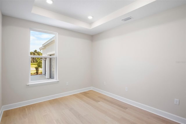 spare room with a tray ceiling, plenty of natural light, and light hardwood / wood-style flooring