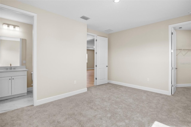 unfurnished bedroom featuring sink, ensuite bath, a spacious closet, light colored carpet, and a closet