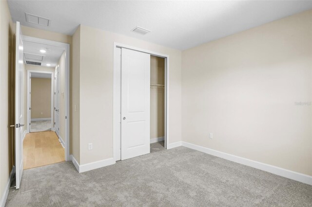 unfurnished bedroom with light colored carpet and a closet