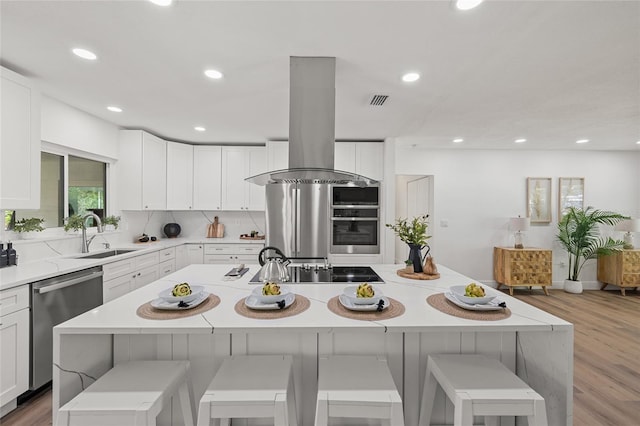 kitchen with a breakfast bar, a center island, appliances with stainless steel finishes, and island range hood