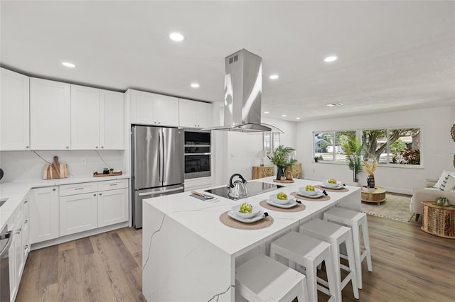 kitchen with white cabinetry, island range hood, stainless steel appliances, and light wood-type flooring