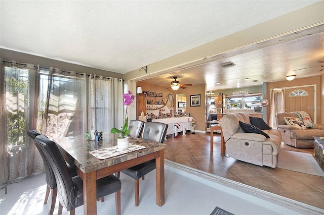 dining space featuring dark tile patterned flooring, ceiling fan, and a textured ceiling