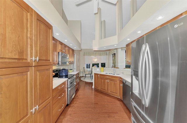 kitchen with ceiling fan, sink, a high ceiling, hardwood / wood-style floors, and appliances with stainless steel finishes