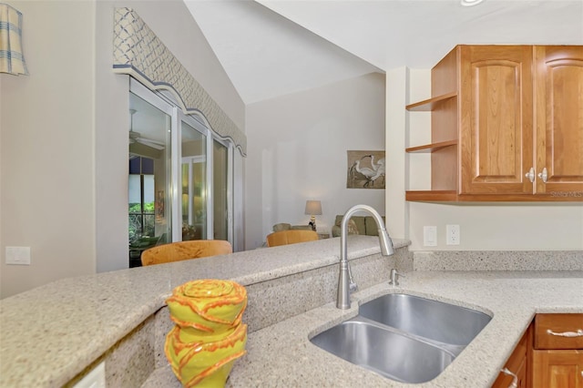 kitchen featuring lofted ceiling, light stone countertops, and sink