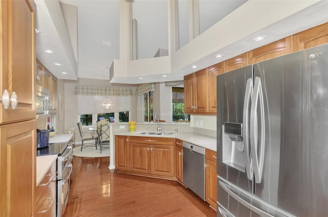 kitchen featuring sink, hanging light fixtures, a chandelier, appliances with stainless steel finishes, and light wood-type flooring