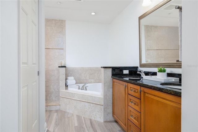 bathroom with wood-type flooring, vanity, and tiled tub