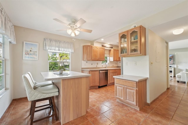 kitchen featuring a kitchen breakfast bar, stainless steel dishwasher, ceiling fan, light tile patterned floors, and a kitchen island