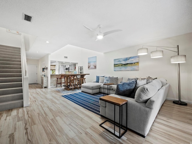 living room featuring ceiling fan, a textured ceiling, and light wood-type flooring