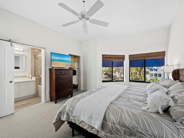 carpeted bedroom with ceiling fan, connected bathroom, and a barn door