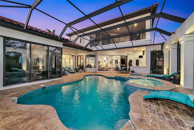 pool at dusk with a lanai, an in ground hot tub, ceiling fan, and a patio