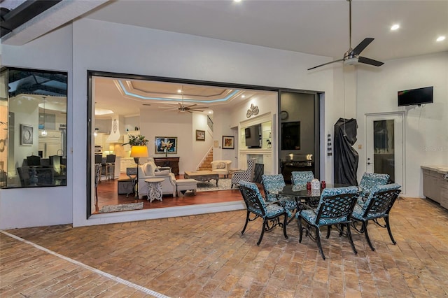 dining area featuring a raised ceiling, crown molding, a fireplace, and ceiling fan