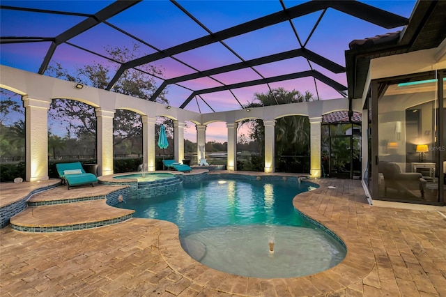 pool at dusk with an in ground hot tub, a patio, and a lanai