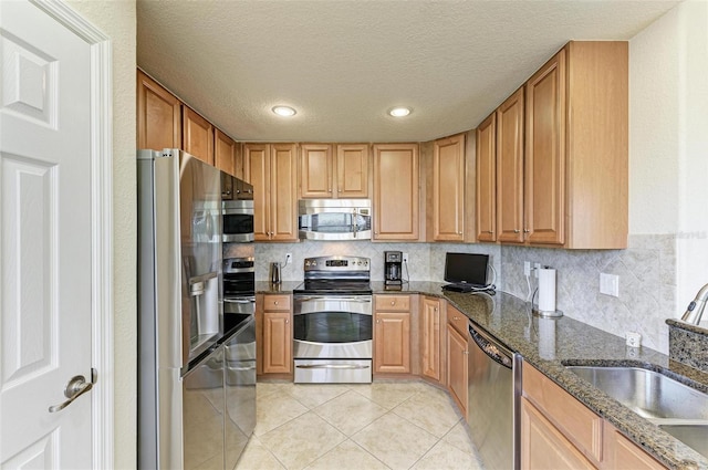 kitchen featuring decorative backsplash, a textured ceiling, stainless steel appliances, sink, and dark stone countertops