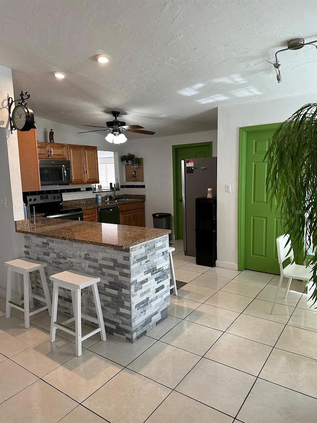 kitchen featuring kitchen peninsula, dark stone counters, sink, black appliances, and light tile patterned floors