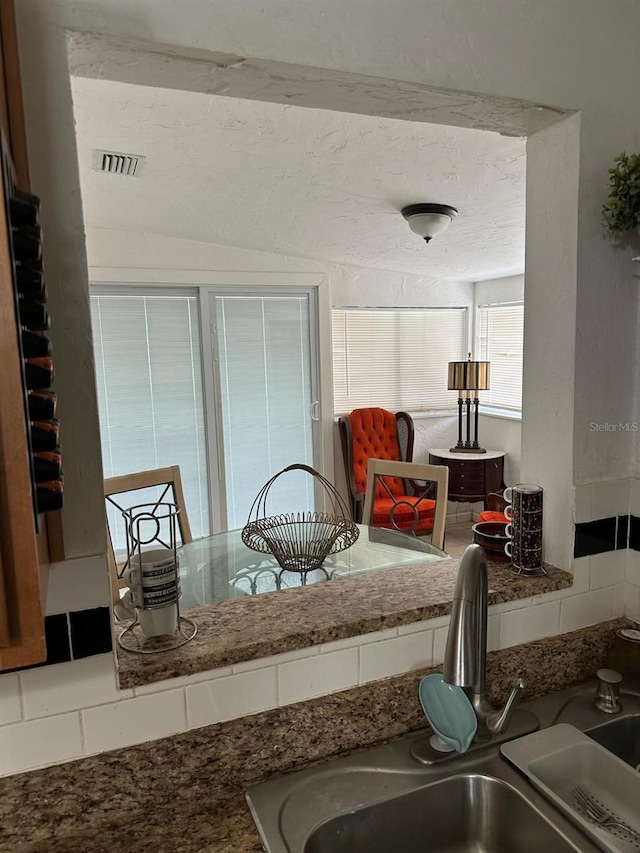 interior space with backsplash, stone countertops, and sink