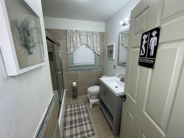 full bathroom with tile patterned floors, vanity, shower / bath combination with glass door, tile walls, and toilet