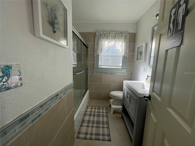 full bathroom featuring vanity, tile patterned floors, combined bath / shower with glass door, toilet, and tile walls