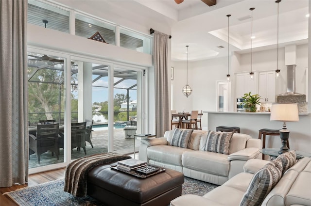 living room with a raised ceiling, ceiling fan, a towering ceiling, and hardwood / wood-style flooring