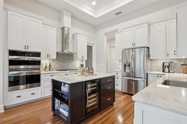 kitchen with wall chimney exhaust hood, beverage cooler, stainless steel appliances, and white cabinetry