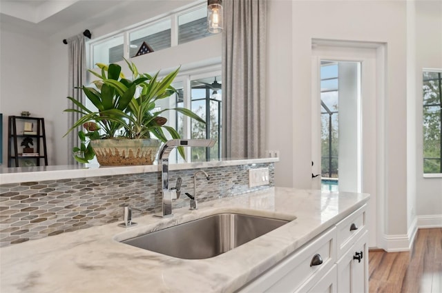 kitchen with light stone counters, sink, white cabinets, and light hardwood / wood-style floors