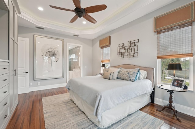 bedroom featuring ceiling fan, dark hardwood / wood-style floors, a tray ceiling, and connected bathroom