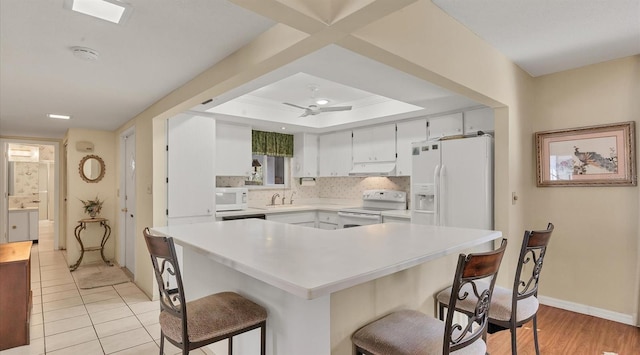 kitchen with ceiling fan, sink, backsplash, white appliances, and a kitchen bar