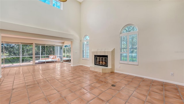 unfurnished living room with light tile patterned floors, a towering ceiling, plenty of natural light, and a premium fireplace