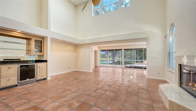 unfurnished living room featuring a towering ceiling, wine cooler, plenty of natural light, and a tiled fireplace