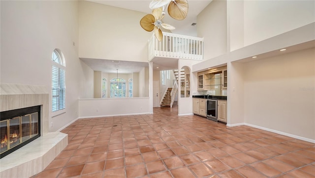 unfurnished living room featuring wine cooler, ceiling fan, a towering ceiling, and light tile patterned floors