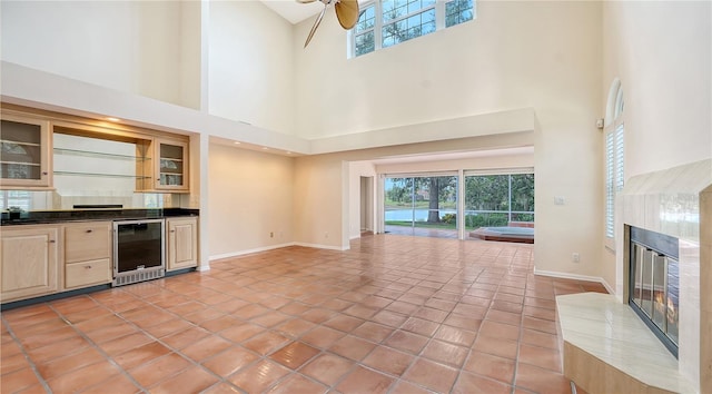 unfurnished living room featuring plenty of natural light, beverage cooler, a high ceiling, and a tiled fireplace