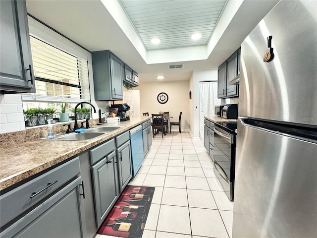 kitchen with a tray ceiling, light tile patterned floors, stainless steel appliances, visible vents, and a sink