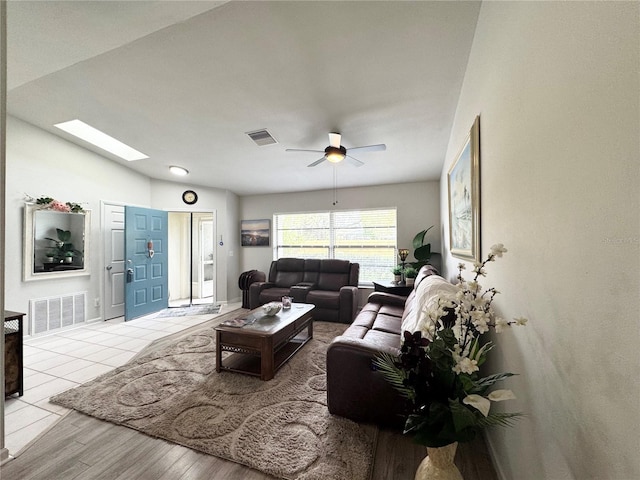 living room with lofted ceiling with skylight, visible vents, ceiling fan, and wood finished floors