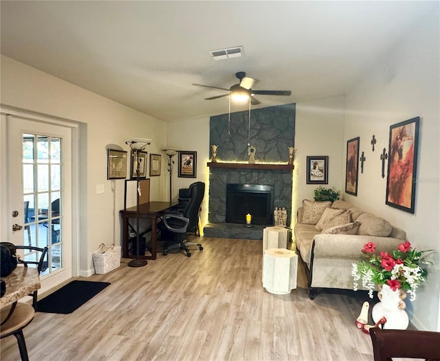 living room featuring lofted ceiling, a stone fireplace, wood finished floors, visible vents, and a ceiling fan