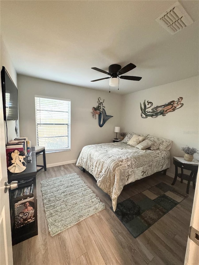 bedroom featuring a ceiling fan, visible vents, and wood finished floors