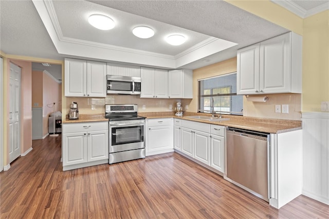 kitchen featuring a tray ceiling, white cabinets, and appliances with stainless steel finishes