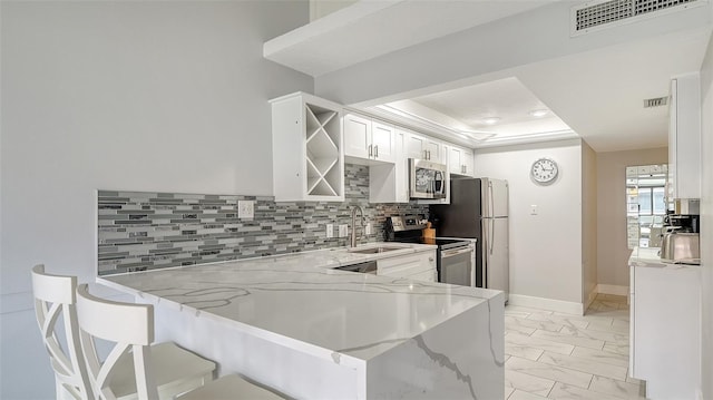 kitchen with white cabinets, decorative backsplash, appliances with stainless steel finishes, light stone counters, and kitchen peninsula