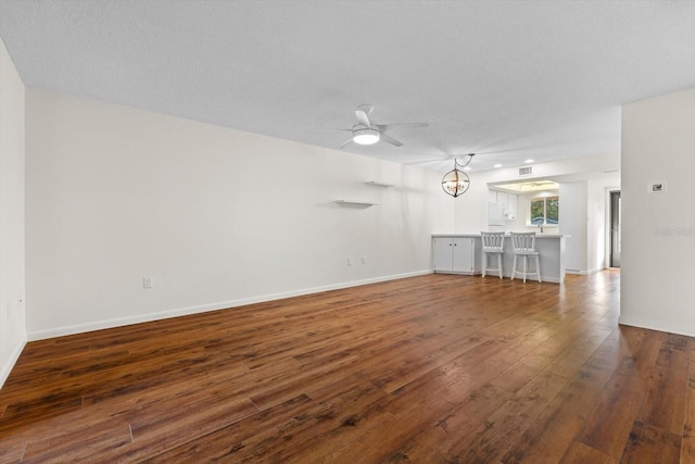 unfurnished living room featuring ceiling fan with notable chandelier, a textured ceiling, and dark hardwood / wood-style flooring