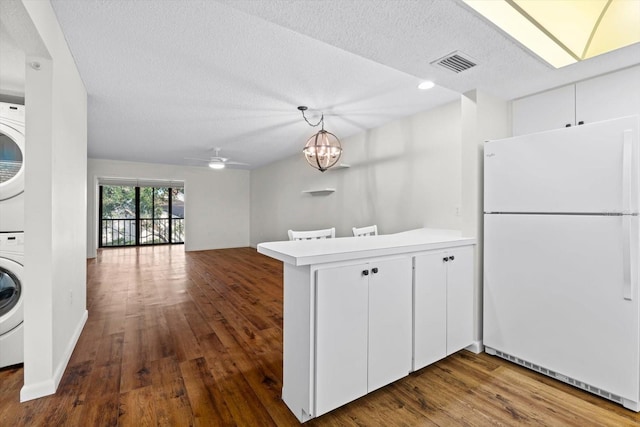 kitchen featuring hanging light fixtures, white cabinetry, stacked washing maching and dryer, white fridge, and kitchen peninsula