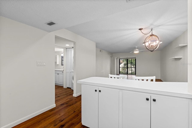 kitchen with kitchen peninsula, ceiling fan with notable chandelier, pendant lighting, dark hardwood / wood-style floors, and white cabinetry