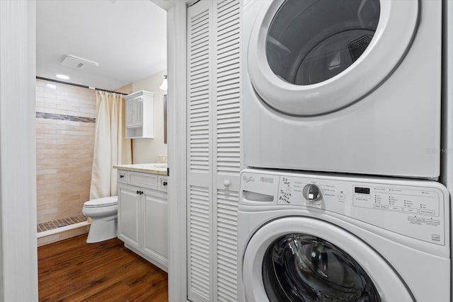 clothes washing area featuring dark wood-type flooring and stacked washer and clothes dryer