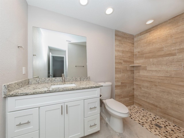 bathroom featuring a tile shower, vanity, and toilet