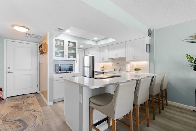 kitchen with white cabinets, sink, light hardwood / wood-style flooring, kitchen peninsula, and stainless steel appliances