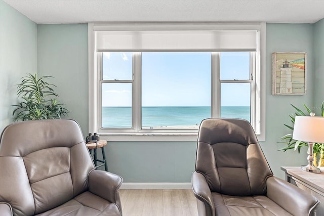 sitting room with a textured ceiling, light wood-type flooring, and a water view