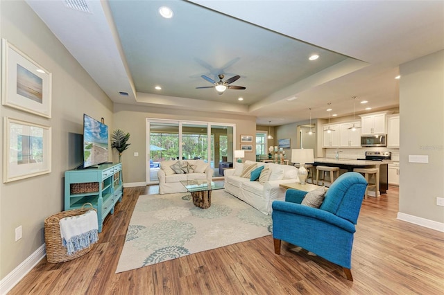 living room with a tray ceiling, ceiling fan, and light hardwood / wood-style floors