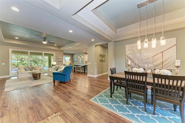 dining room with hardwood / wood-style floors, a raised ceiling, and ceiling fan