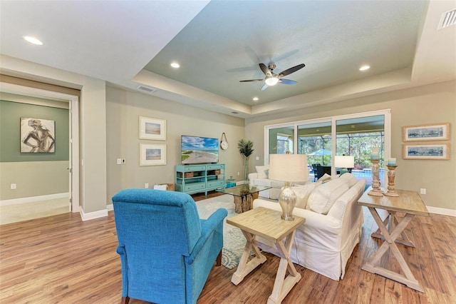 living room with a tray ceiling, ceiling fan, and light wood-type flooring