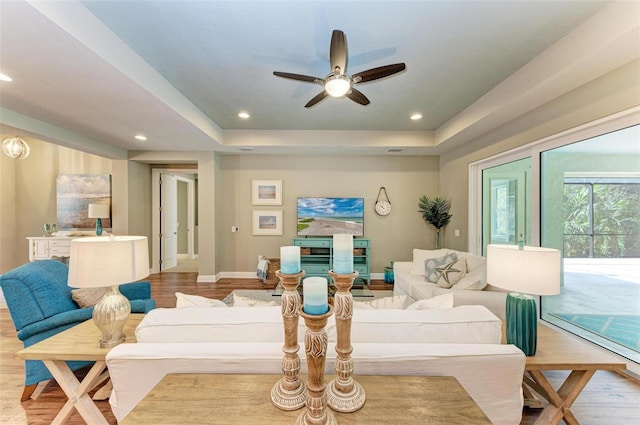 living room with a raised ceiling, ceiling fan, and light hardwood / wood-style flooring