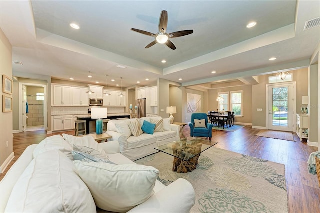 living room featuring hardwood / wood-style flooring, a raised ceiling, and ceiling fan